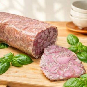 Apetyczne zbliżenie na wiejski salceson wieprzowy podawany na drewnianej desce. Całe bloki i gruby stos plastrów pokazują tradycyjną teksturę, udekorowane świeżym rozmarynem i otoczone solą oraz musztardą. Wykwintny wybór dla miłośników delikatesów i diety keto.